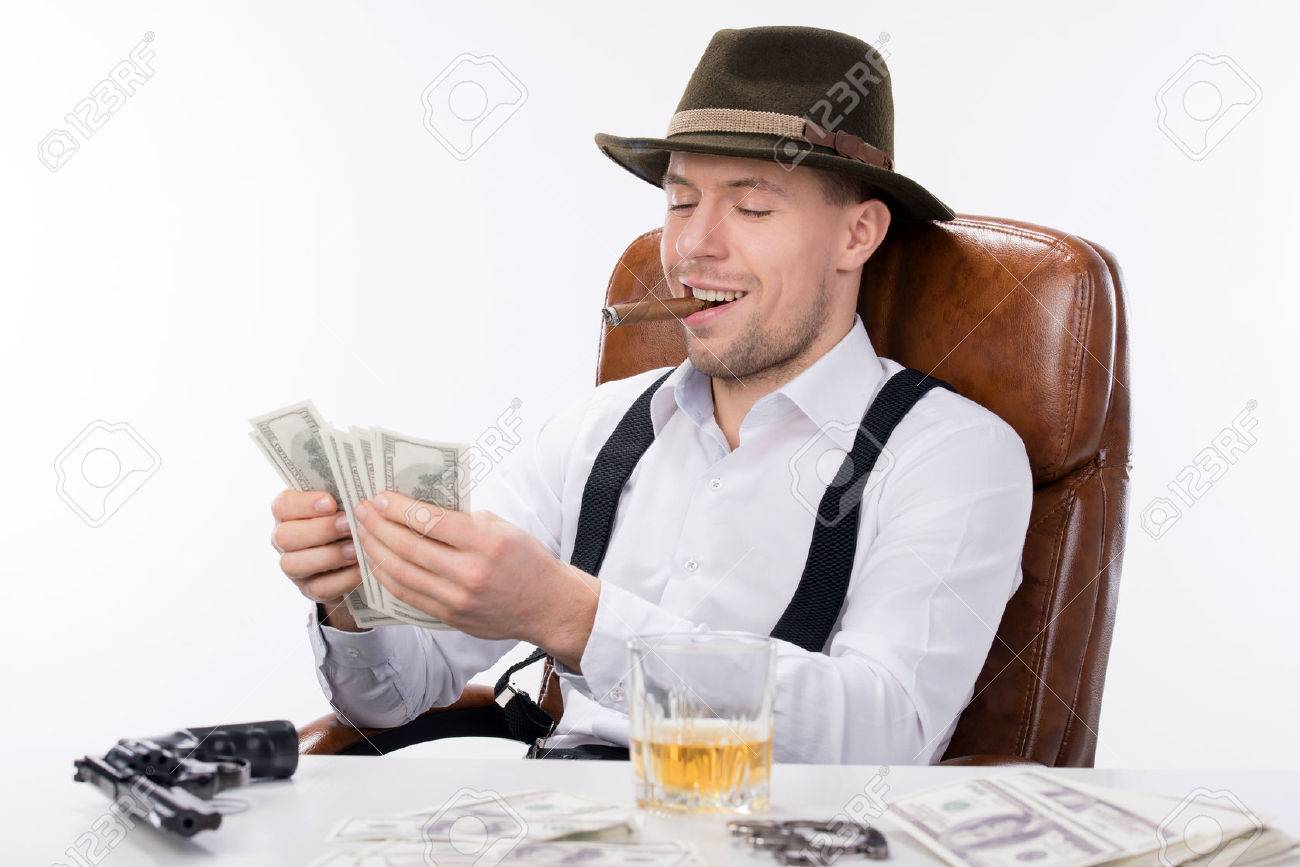 26329513-gangster-sitting-at-a-table-counting-money-on-the-table-gun-and-brass-knuckles-Stock-Photo.jpg